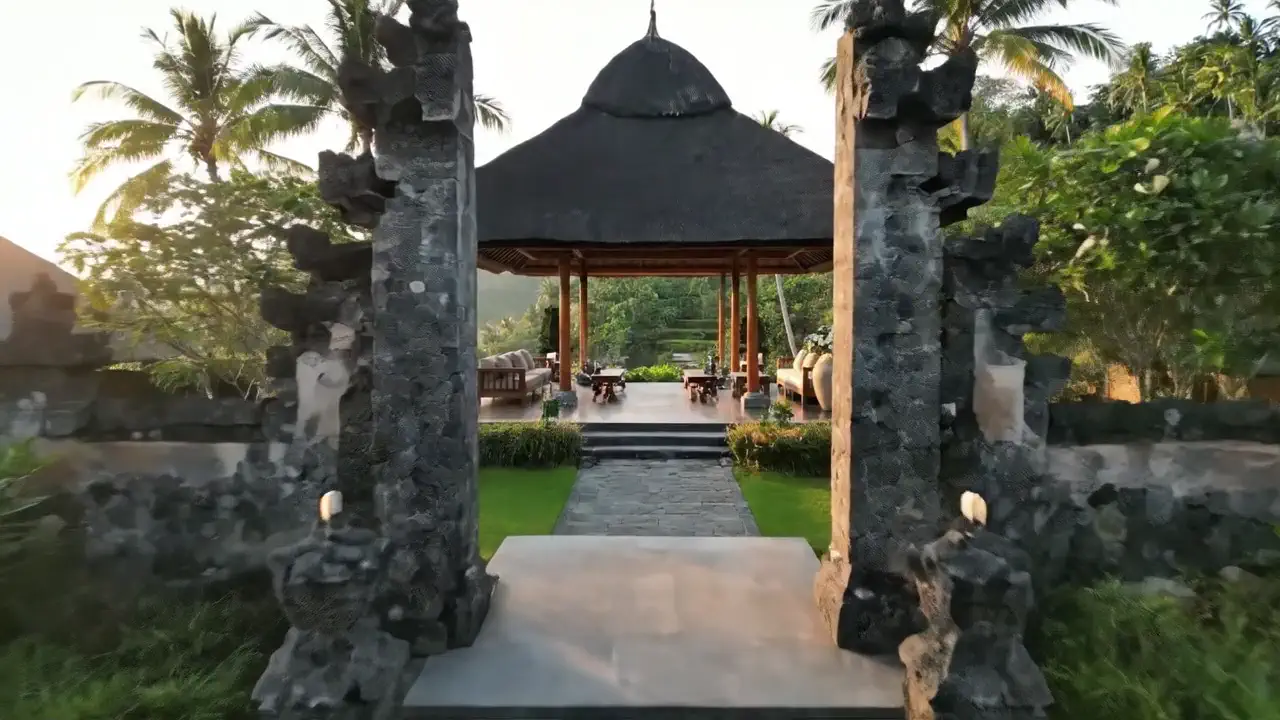 A carved stone gate, split down the middle, framing a path to an open pavilion.