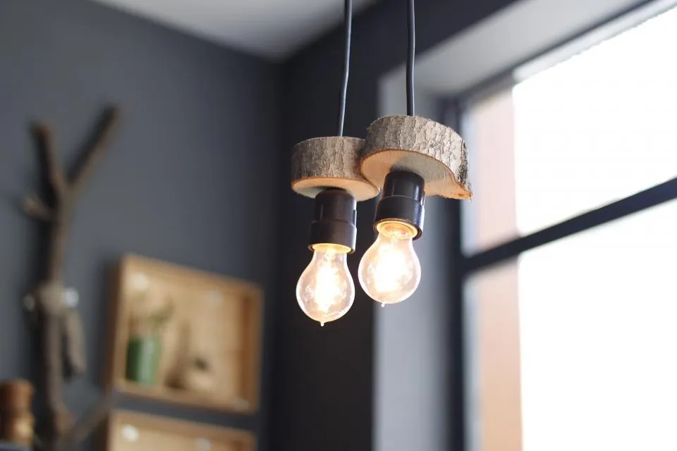 Two bare bulbs hanging from wooden pendants in a dark grey corner by a window.