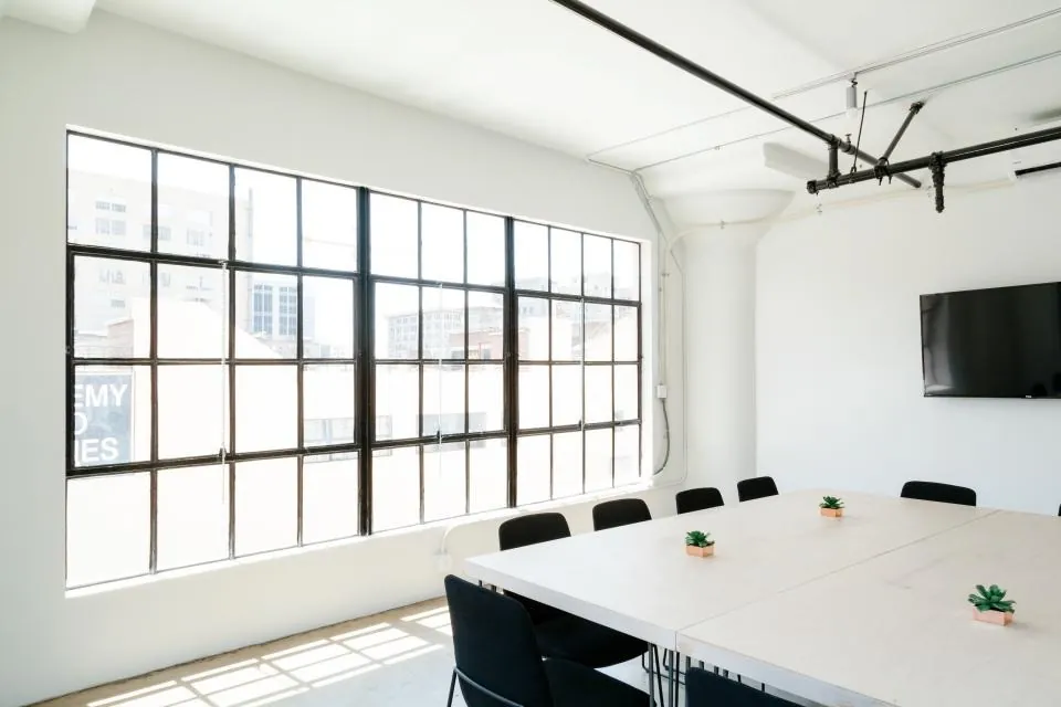 A loft room with a wall of black-framed windows, a long white table and black chairs.