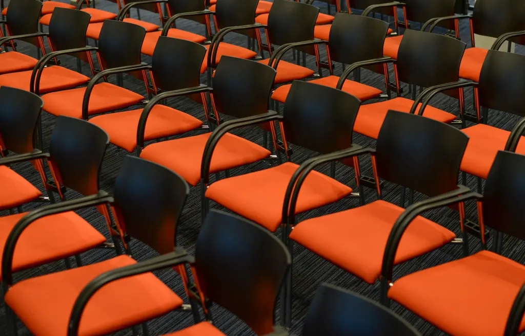 Rows of orange and black chairs in an empty talk room.