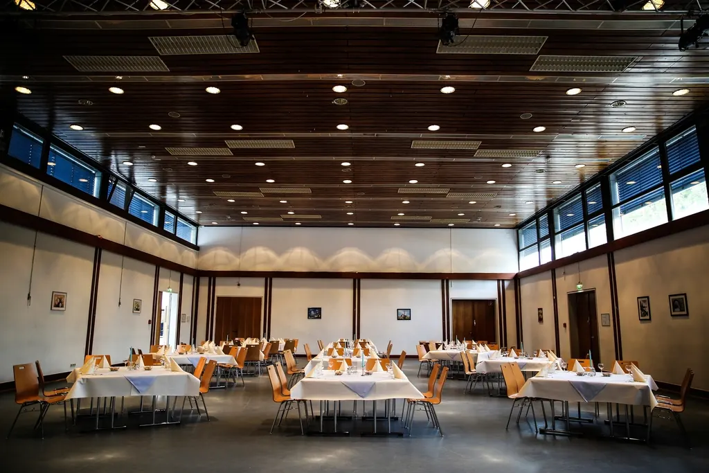 A long hall set with round tables and white tablecloths under a wooden ceiling.