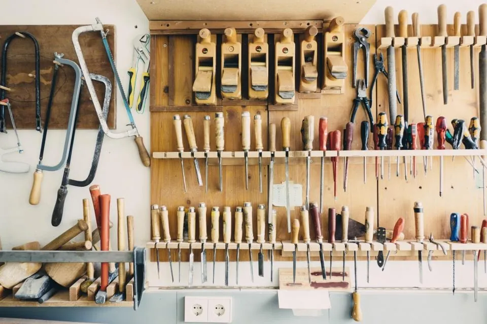 A workshop wall with rows of chisels, saws, screwdrivers and planes hanging in order.
