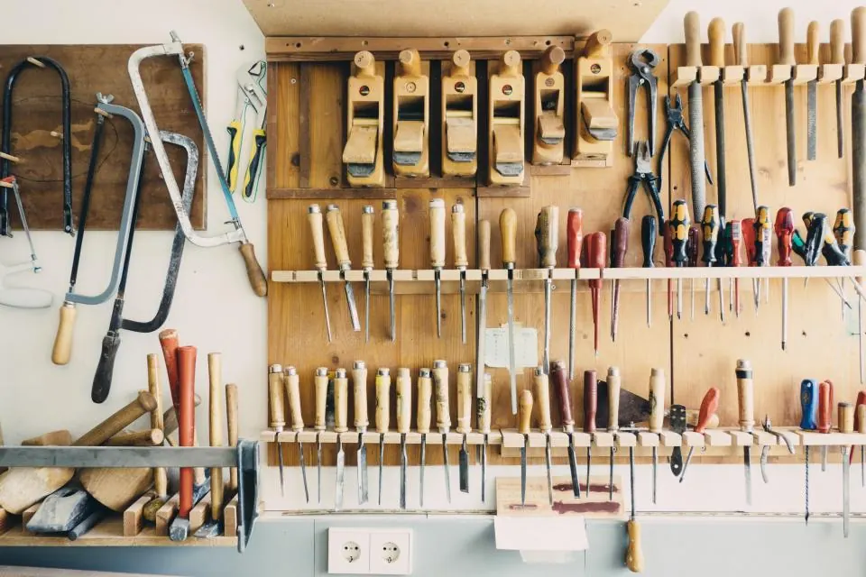 A workshop wall with rows of hand planes, saws, chisels and screwdrivers hung neatly on wooden racks.