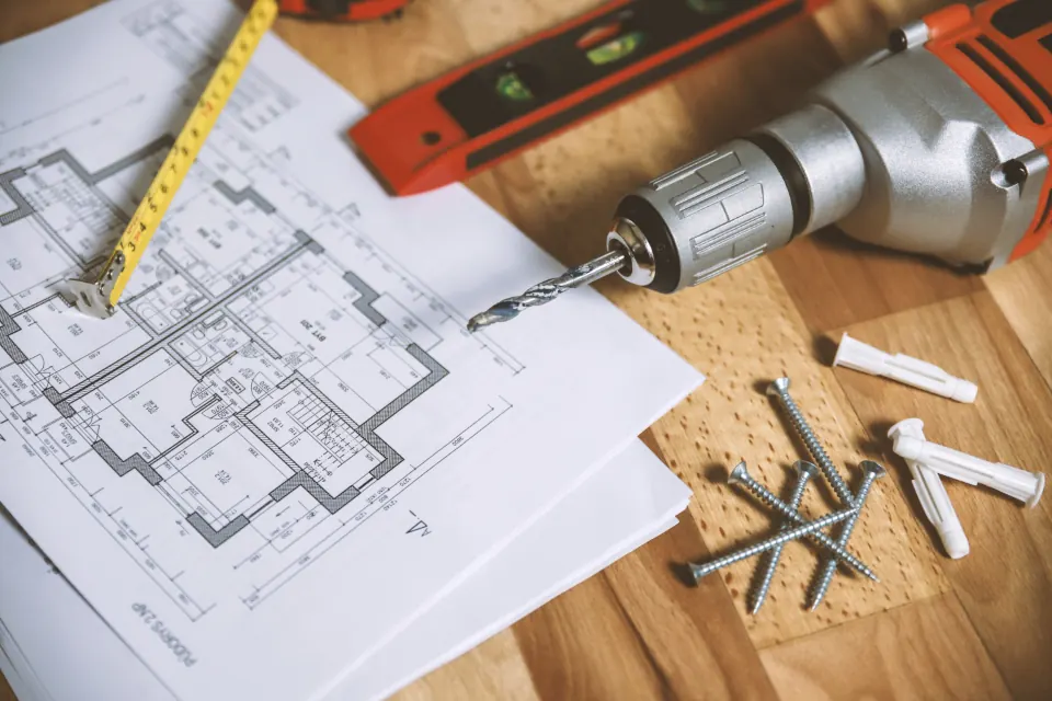 A cordless drill, a spirit level and screws on top of a printed floor plan.