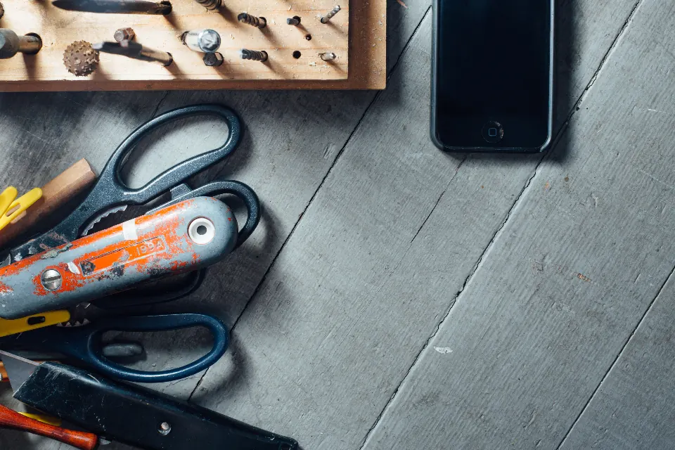 Scissors, a craft knife and small tools on a grey wooden table.