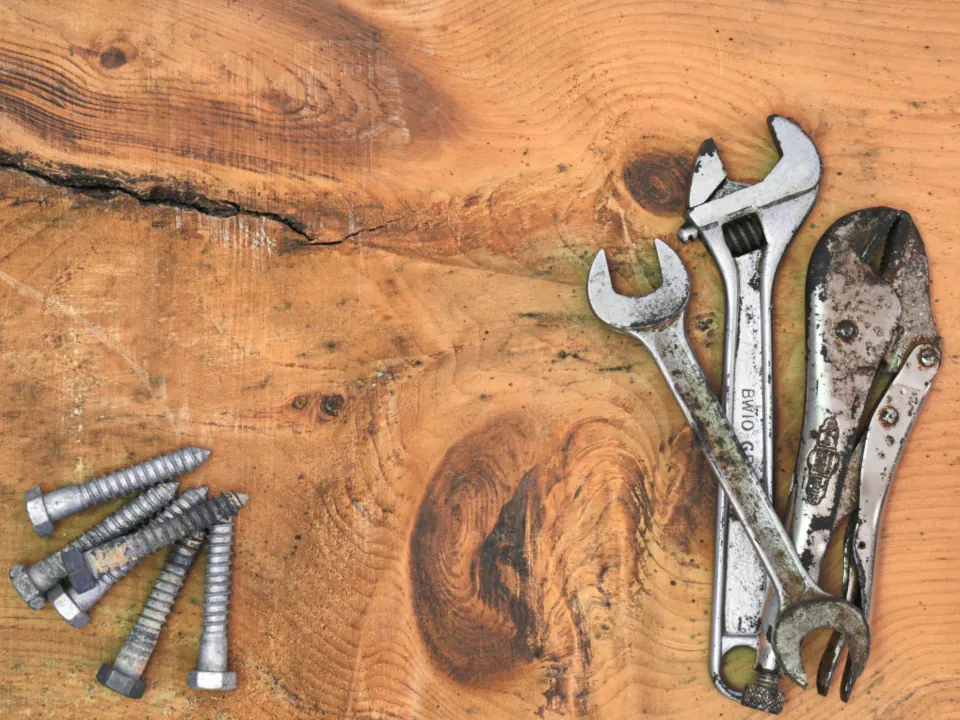 Spanners, a wrench and screws laid out on a wooden bench.