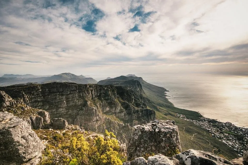 Sea cliffs with green tops falling to a calm sea under a pale, cloudy sky.