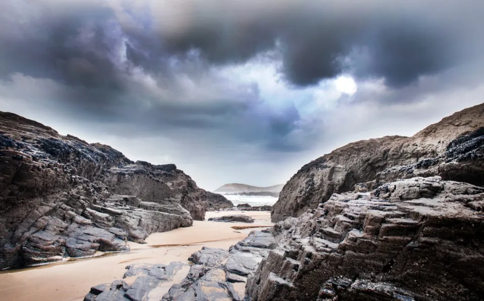 Dark, wet rocks on a beach under heavy storm clouds.