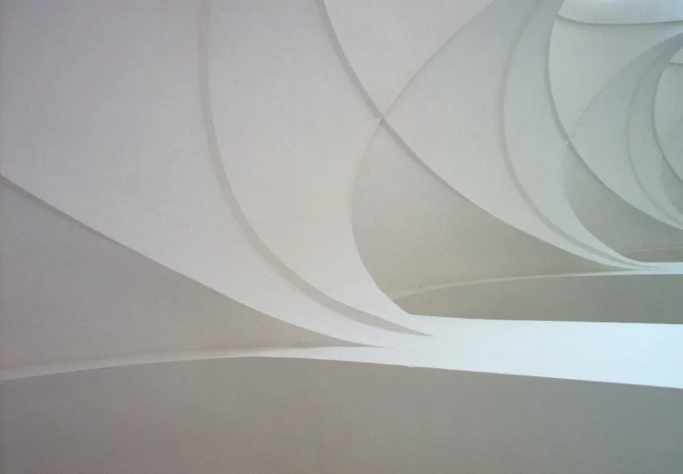Smooth white curved surfaces of a modern building, overlapping in soft light.