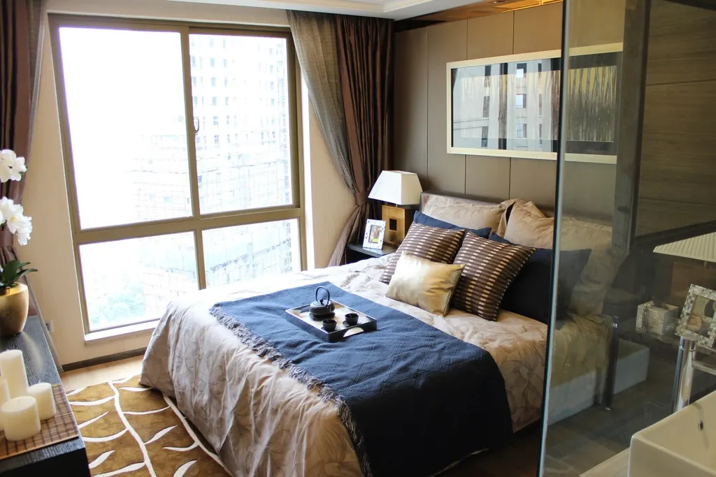 A bedroom with a wide bed, bedside lamps and a large window.