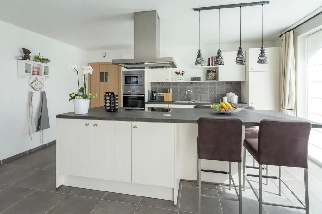 A white kitchen with an island, bar stools and pendant lights.