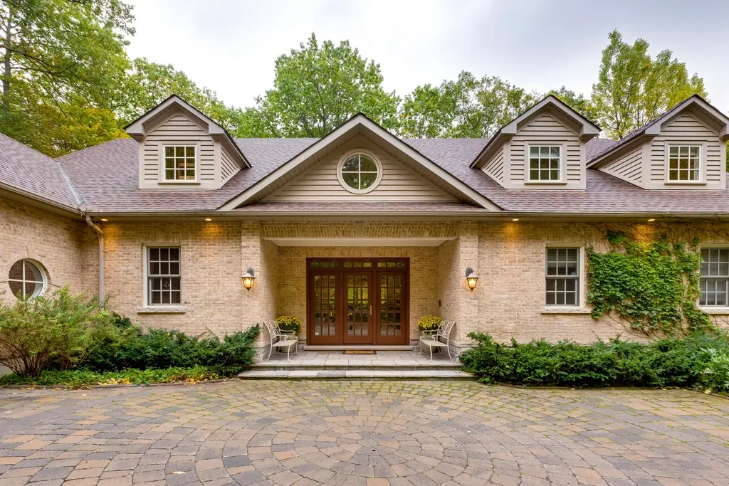 A wide brick house with dormer windows, a wooden door and a paved drive.