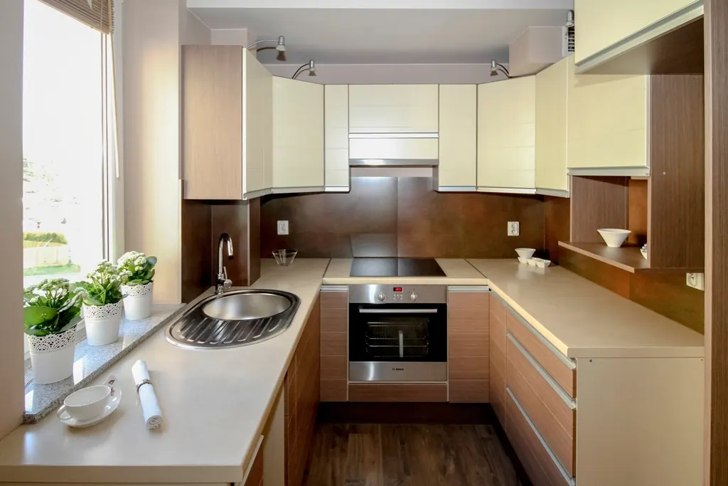 A compact kitchen with pale cabinets, a hob and herbs on the windowsill.