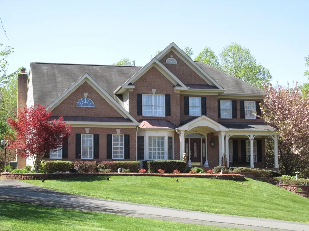 A large brick house with white windows, a lawn and a flowering tree.