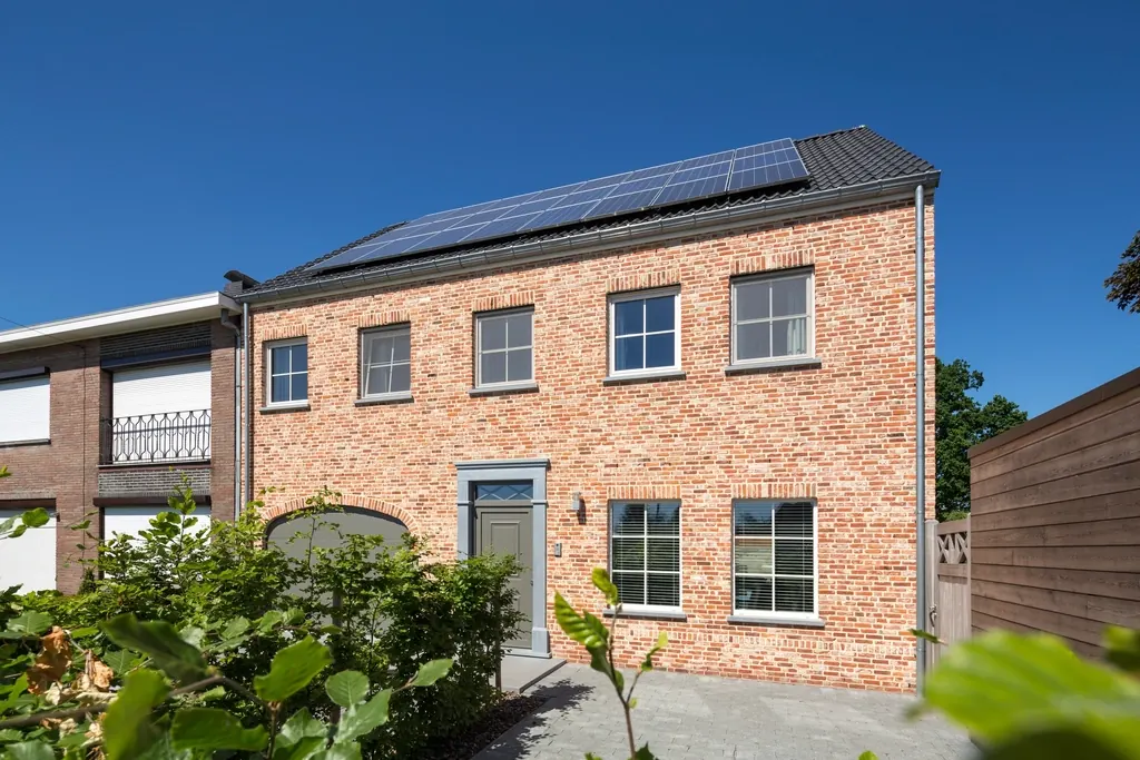 A brick townhouse with large windows and solar panels on the roof.