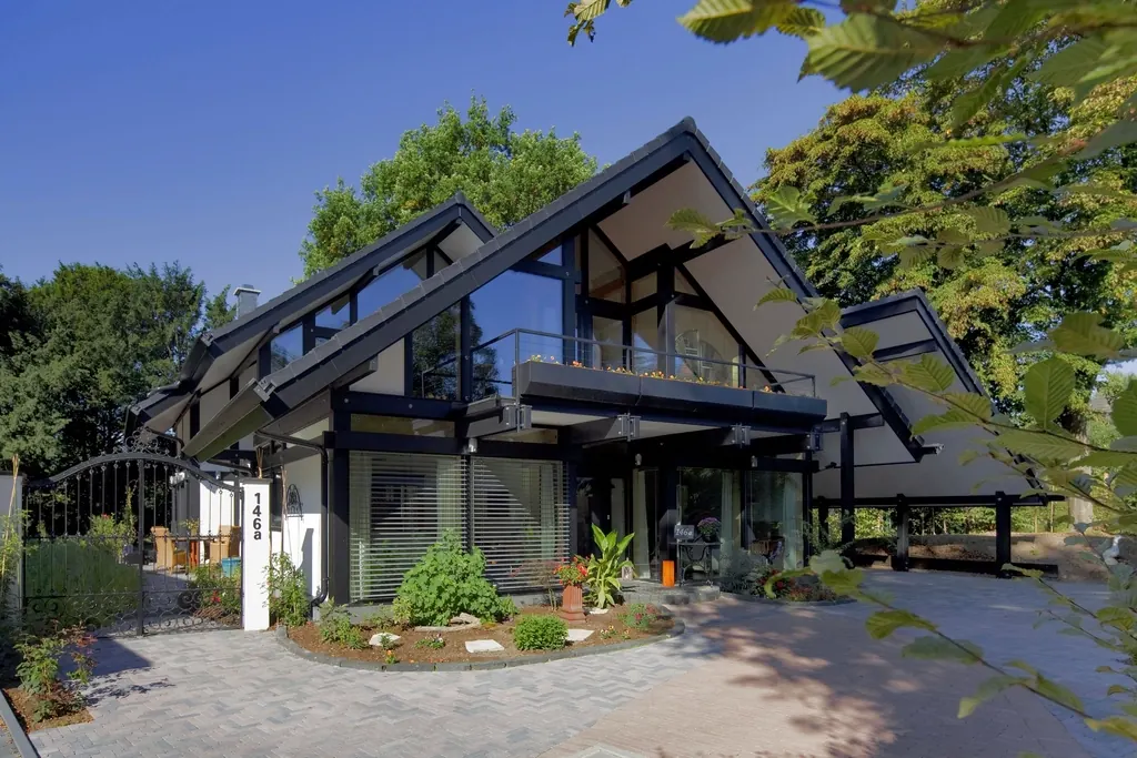 A modern house with a steep roof, tall glass walls and a planted front garden.