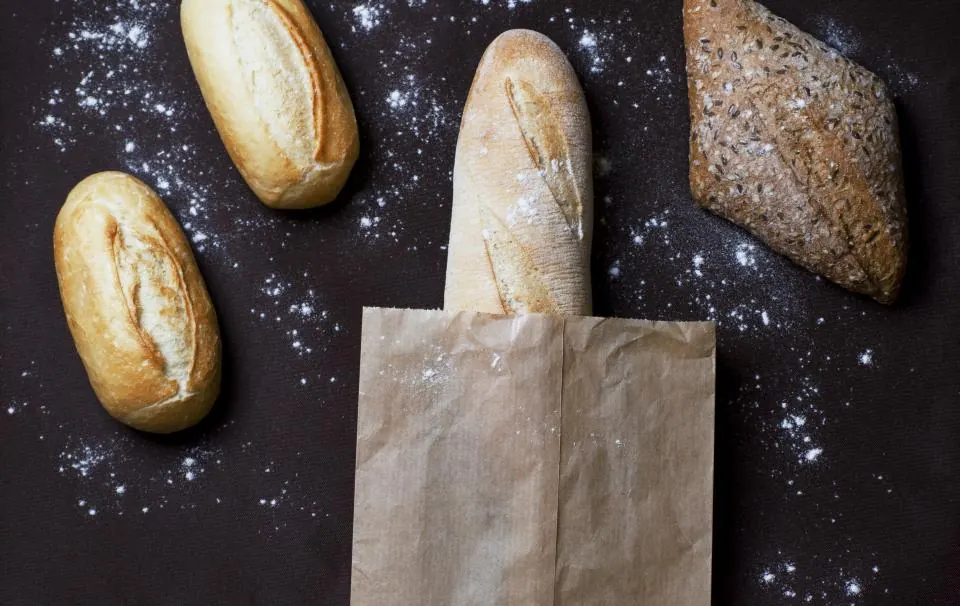 Loaves of sourdough and rye on a bakery shelf with handwritten price cards.