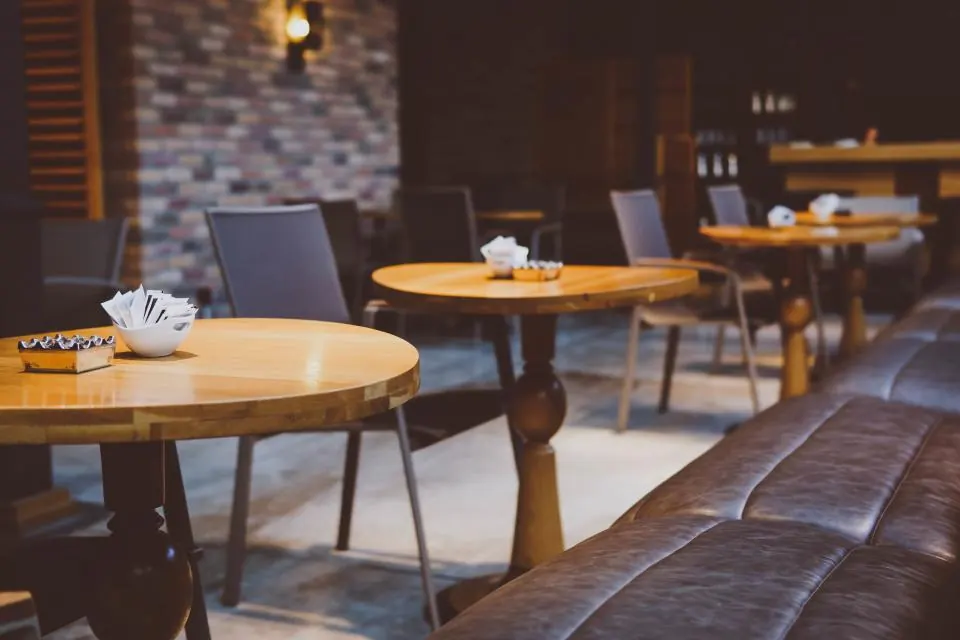 A warm café room with round wooden tables, a leather bench and a brick wall at the back.