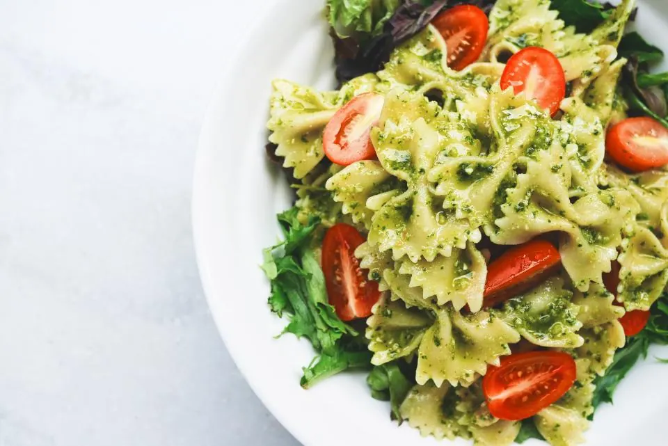 A bowl of bow-tie pasta with pesto, cherry tomatoes and leaves.