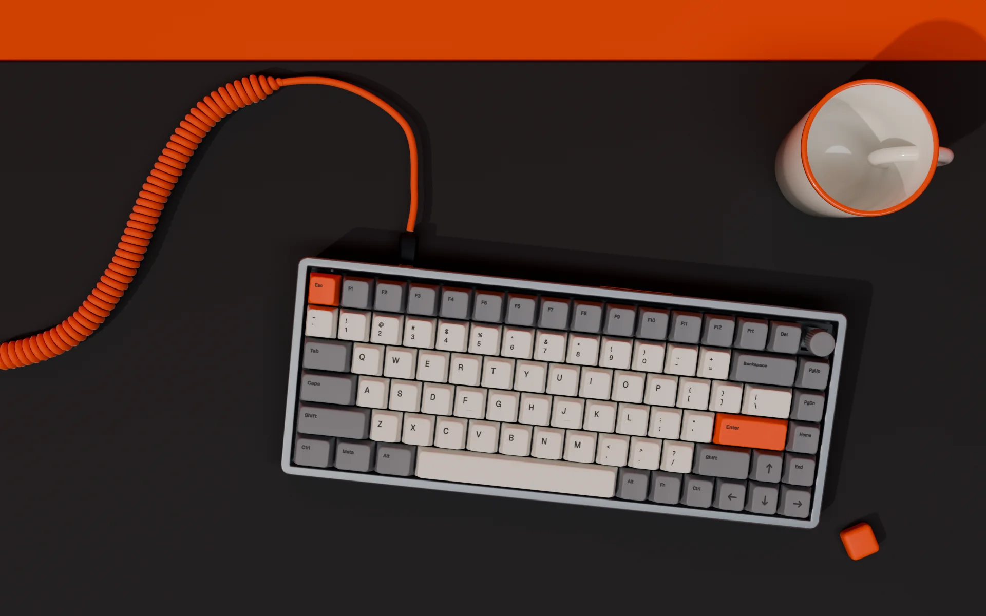 Top view of the Kesten 75 on a graphite felt mat, with an orange coiled cable, a white mug and a spare orange keycap.