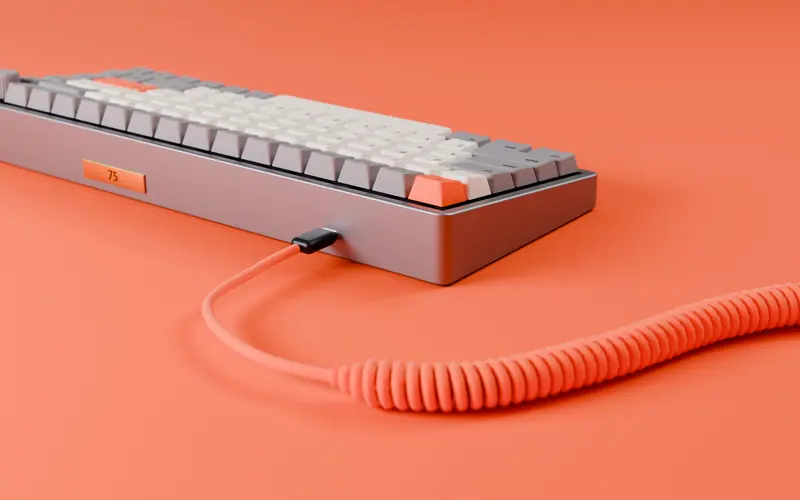 The back of a keyboard with a brass 75 badge and a coiled orange cable.